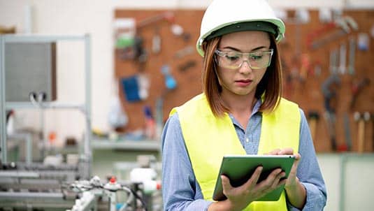 Photo of a person in a hard hat looking at an ipad in a factory.